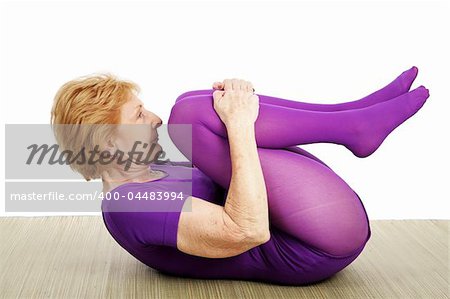 A fit flexible seventy year old woman doing a suppine yoga pose.  White background