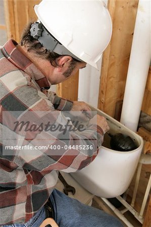 A construction plumber installing a toilet tank in a new building.  Authentic and accurate content depiction.