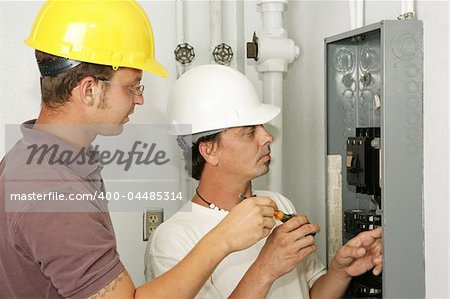 Electricians wiring an electrical breaker panel.  Models are professional electricians - all work depicted is being performed according to industry codes and safety standards.
