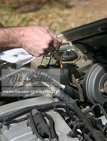 A closeup of a mechanic's hand pulling on the dipstick to check a car's oil.