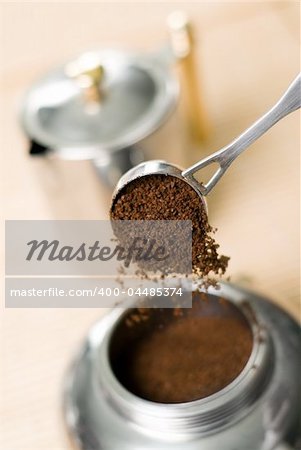 Pouring ground coffee (focus on it) into coffee maker. Shallow depth of field.