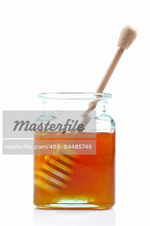 A wooden drizzler inside of honey jar, reflected on white background