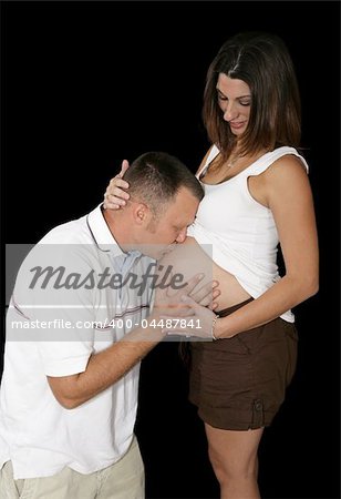 An expectant father kissing his wife's pregnant belly.  Black background.