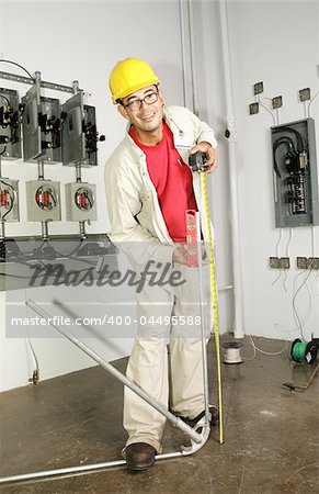 Electrician bending conduit pipe on the job.  Actual electrician performing work according to national code and safety standards.  (writing on bender is instructions, not trademark)