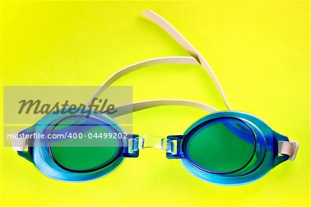 Pair of blue swimming goggles on a yellow background