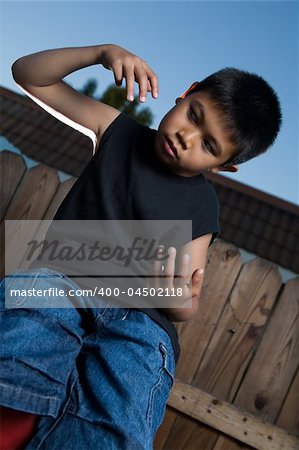 Young asian boy outside beside a tall wooden fence wearing jeans and black tshirt