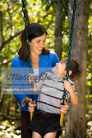 Hispanic mother pushing son on swing and making eye contact.