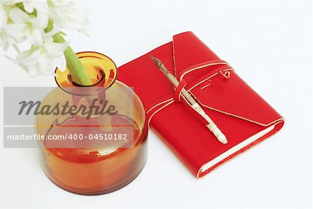 An old red diary with a calligraphy pen on top -  white background