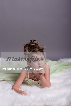 little girl dressed as a princess in evening dress sitting down on white fur