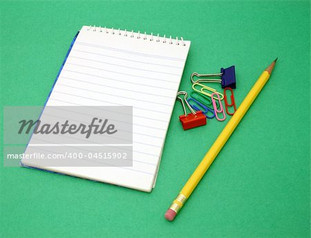 yellow pen and paper clips besides an open notebook on a green surface