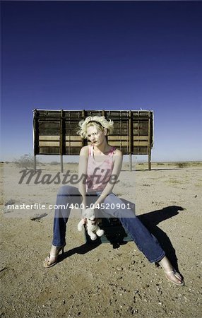 Woman sitting on suitcases in front of an old billboard waiting in the desert.