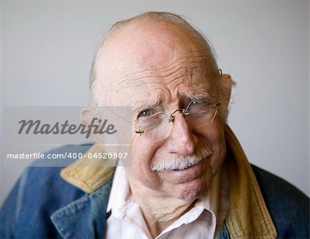 Portrait of a senior citizen wearing glasses and a jean jacket in a studio.