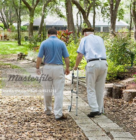 Father and son strolling through the garden together.  The father is in a walker.
