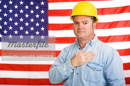 Patriotic american worker with his hand over his heart in front of the US flag.  Photographed in front of flag, not composite image.