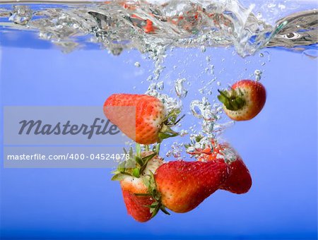 Strawberries falling in blue water with splash and bubbles