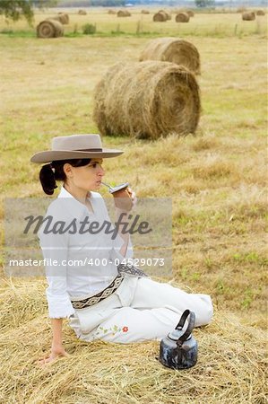 A young Argentinean farm girl relaxes in the field drinking yerba mate