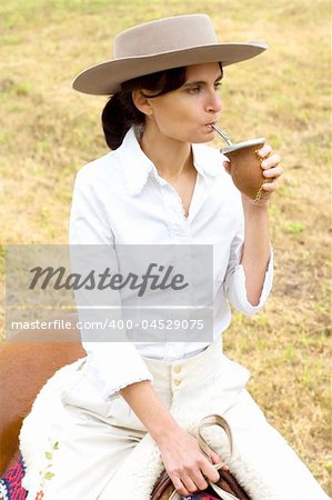 A young Argentinean gaucha relaxing with yerba mate while riding her horse.