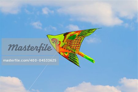 A kite flying against a blue sky in sunlight, bright colors and streaming tail