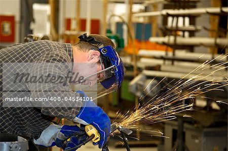 Machinist grinding metal in a factory.  Horizontal with room for text.  Authentic and accurate content depiction in compliance with industry code and safety standards.