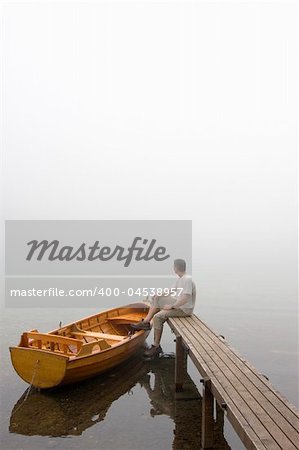 Man sitting on a landing stage at a misty morning in fall