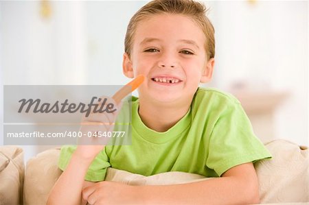 Young boy eating carrot stick in living room smiling