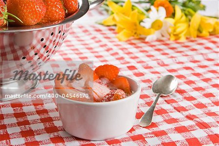 Sliced strawberries and cream in a white pot with flowers in the background