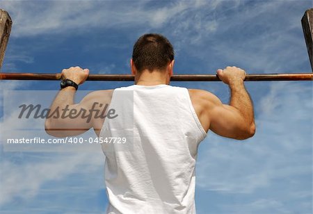 Reaching Goal: Strong Man Doing Pull-ups on a Bar in a Park