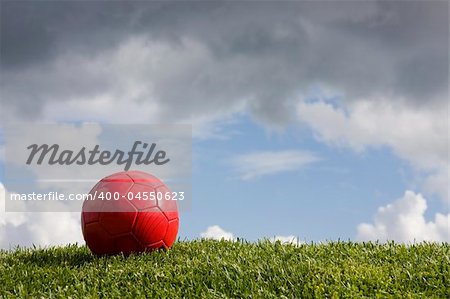 A football red ball on the grass witha cloudy sky