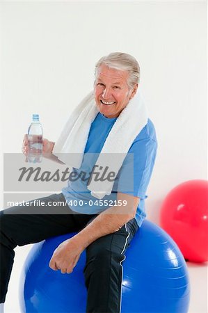 senior adult sitting on fitness ball in gym and holding water bottle