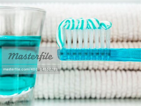A blue toothbrush with toothpaste, a glass full of mouthwash and towels on the background.