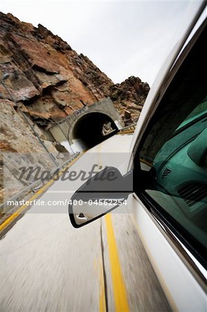 car approaching tunnel through the mountains. Focus on mirror, motion blur on road.