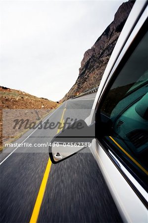car travel through mountains, focus on mirror and motion blur on road