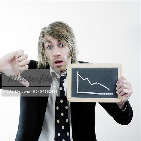 Businessman with a look of surprise, a thumb down sign with his right hand, and holding a small chalkboard with a down trend graph in the other.  Isolated on white background.