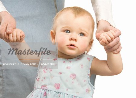 The smiling little girl in a blue dress hold on mum's hands and tries to go