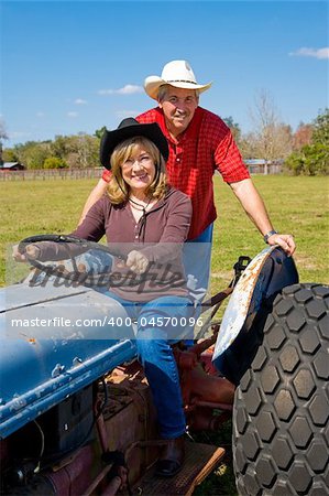 Mature married couple riding the tractor on their farm.