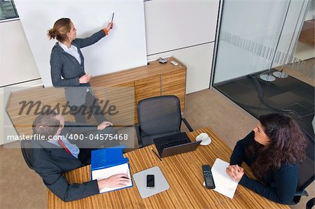 Three young business associates in a meeting, one presenting a theory in front of a white screen.