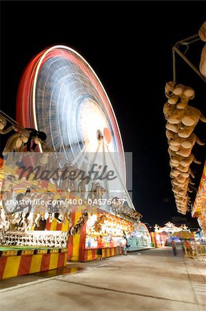 A night view of a Carnival with a Ferris Wheel and various games with toys.