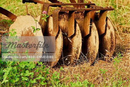 Vintage farm equipment, harrow, with five steel discs coverd with clay and rust.