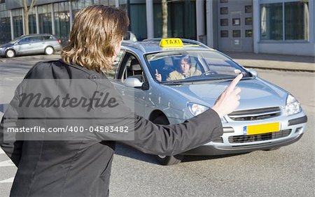 A businessman raising his hand to haul a passing taxi. The driver acknowledges, but speeds on. Slight motion blur in the taxi