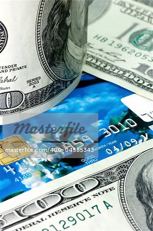 Blue credit card lying upon hundred dollars bills