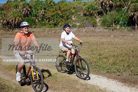 Happy senior couple riding their bikes through the park.