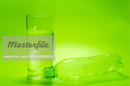 Glass of water and empty bottle on green background