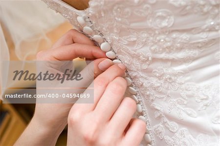 hands of a person help to a bride to clasp buttones of the dress