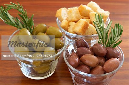 Two jars of green and black olives with stick of rosemary and croutons on wooden table background