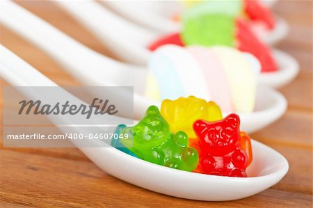 Assortment of candies in the spoons with soft shadow in the wooden background. Shallow depth of field