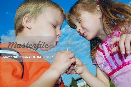 two kids blowing dandelion seeds together wishing
