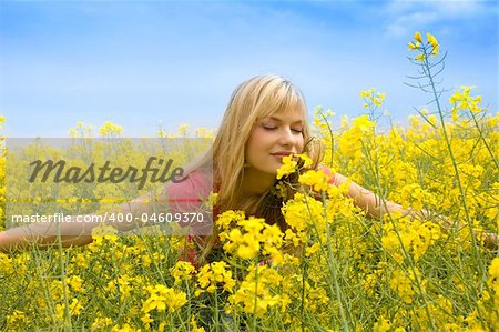 happy blond girl with open arms smelling some flowers in a yellow field