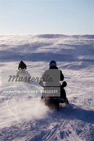 Two people riding up a hill on snowmobiles
