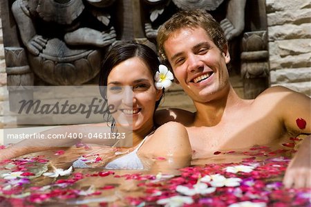 A young couple together in a bath with petals and flowers at a tropical spa