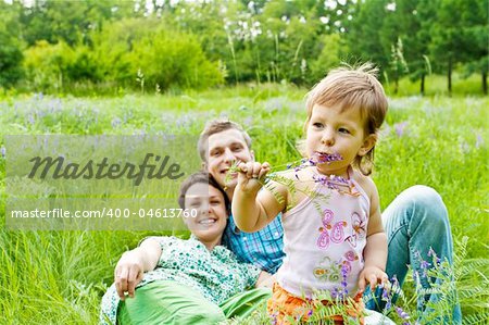 Lovely toddler eating flower, smiling parents in back